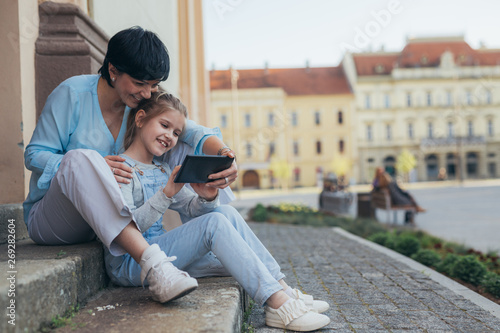 little girl with her mother using tablet outdoor in the city