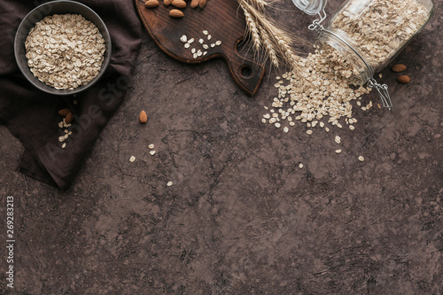 Full bowl of dry oatmeal flakes with ears of wheat and almond nuts on dark background. Cooking oats porridge concept. Free space for text. Top view photo