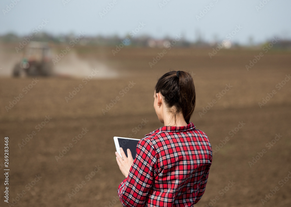 Farmer woman with tablet and tractor in field