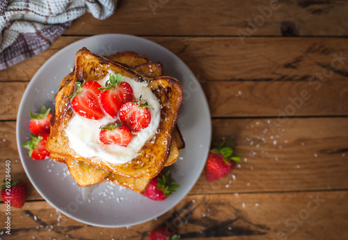 French toast with fresh strawberries, coconut shreds and honey, on wooden background, top view, text space, copy space