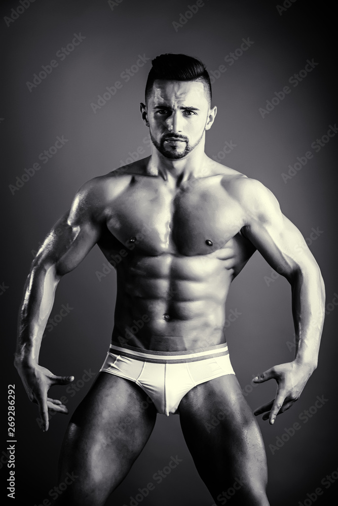 Man posing in the studio on a dark background. Bodybuilder and active lifestyle. Seductive and strip theme. Attractive man with pumped biceps and stomach muscles.
