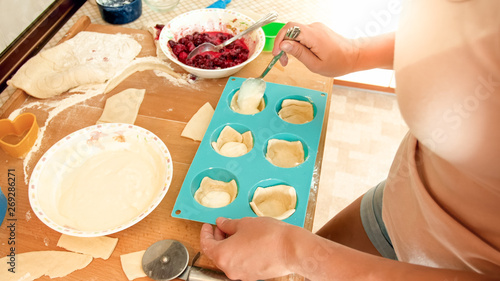 Closeup image of young woman making cupcakes. Girl putting creme inside of the dough in silicone forms for baking