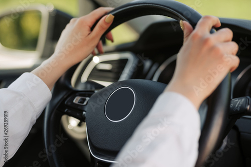 Woman's hands holding on black steering wheel while driving a car.