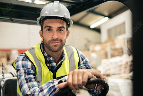 Fotografie, Obraz Smiling warehouse worker sitting in a forklift