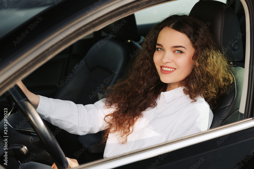Close up portrait of pleasant looking female with glad positive expression, being satisfied with unforgettable journey by car, sits on driver`s seat, enjoys music. People, driving, transport concept Close up portrait of pleasant looking female with glad positive expression, being satisfied with unforgettable journey by car, sits on driver`s seat, enjoys music. People, driving, transport concept