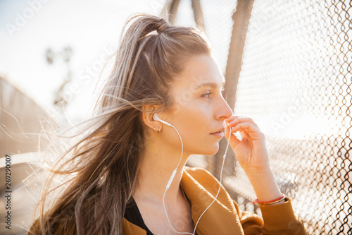 Foto Pensive young woman listening music on earphones while looking through fence