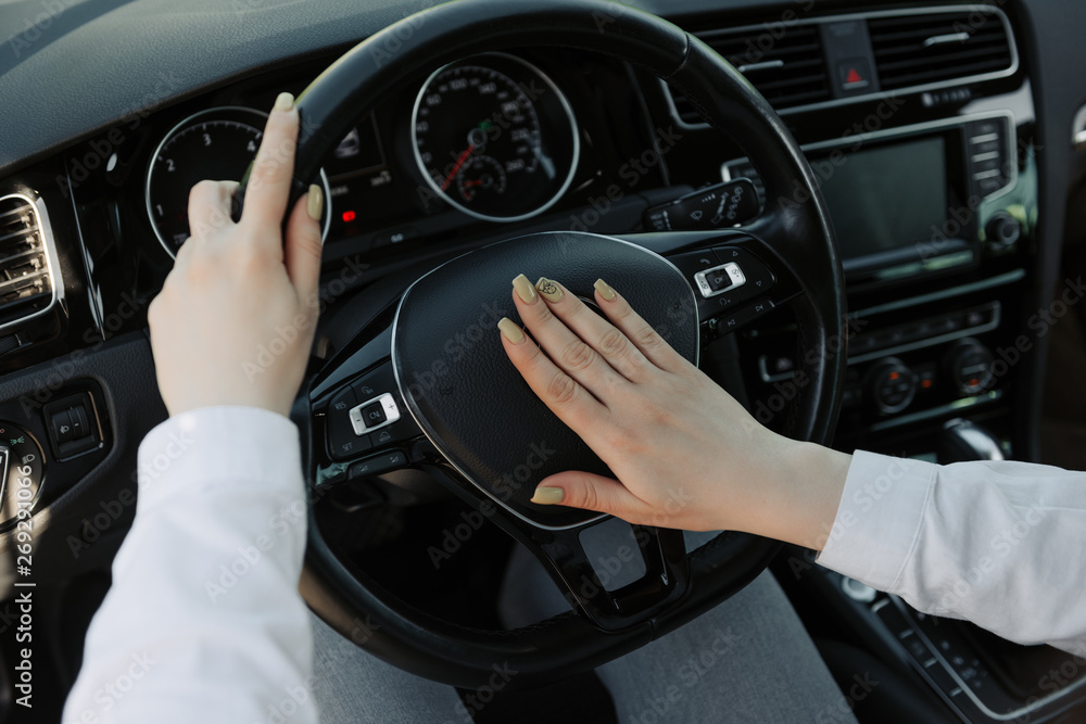 Close up of a women is hands holding a car's steering wheel and honking the horn.