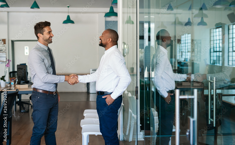 Obraz premium Two laughing businessmen shaking hands together after an office meeting