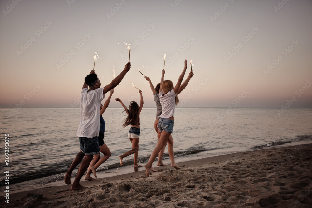 Fototapeta premium Happy smiling friends running at the beach with sparkling candles