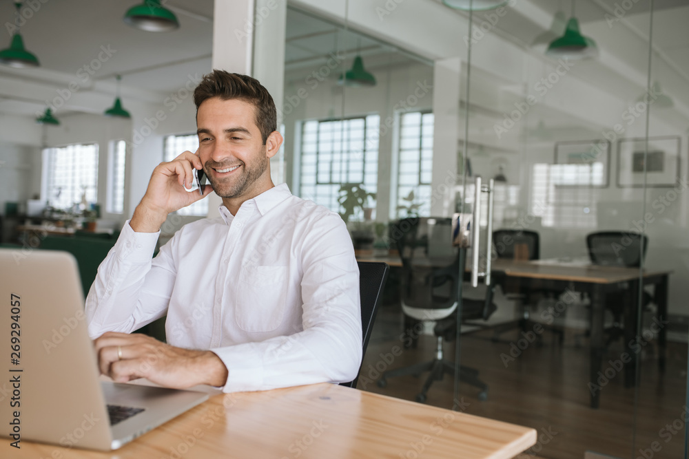 Smiling businessman talking on a cellphone and using his laptop Smiling businessman talking on a cellphone and using his laptop