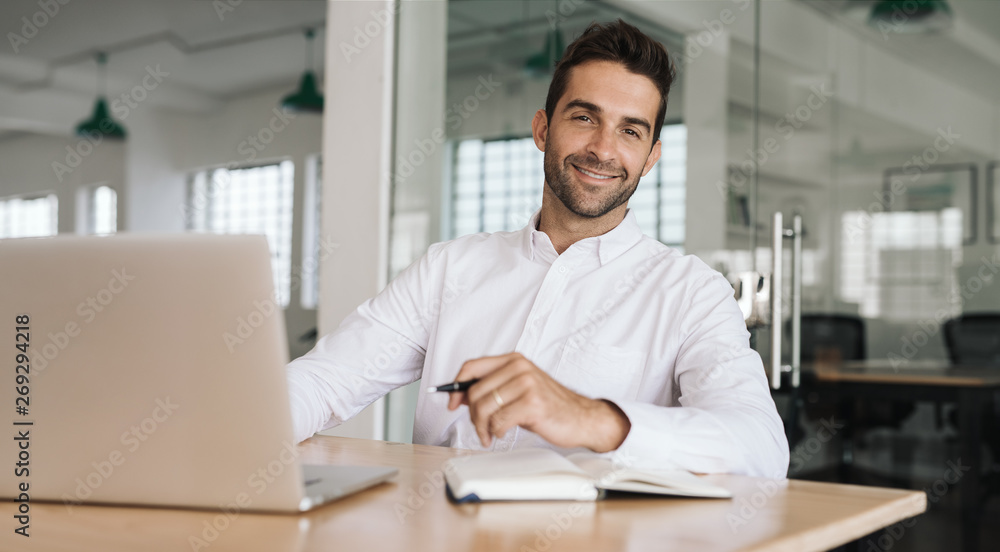 Smiling businessman writing down notes while working on a laptop