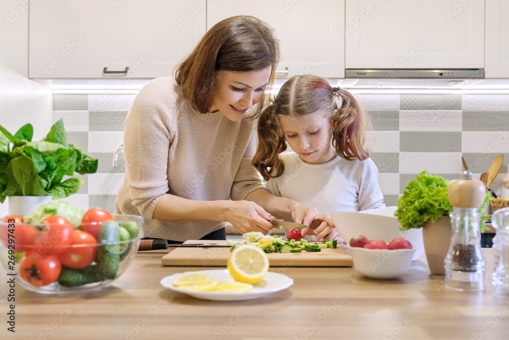 Mother and child cooking together at home in kitchen. Healthy eating, mother teaches daughter to cook