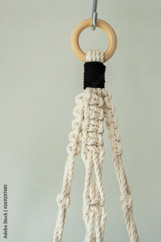 A hand-made macrame plant hanger made using 100% natural cotton. This is the top of the macrame. The wooden ring is shown.