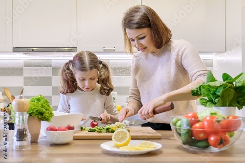 Mother and daughter cooking together in kitchen vegetable salad, parent and child are talking smiling.