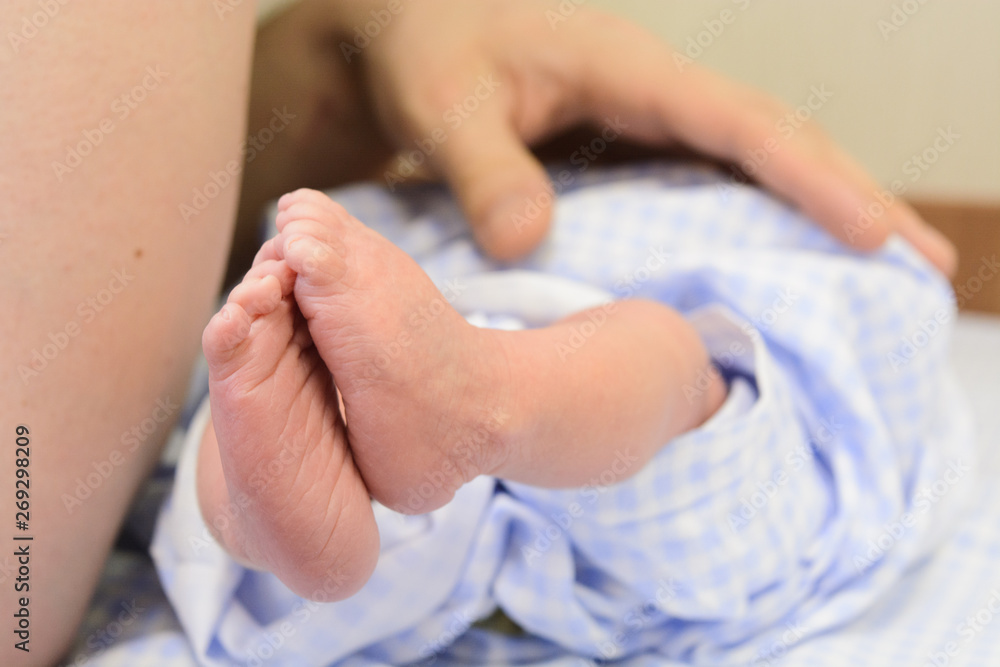 Small newborn baby feet in blue nappy with man hand