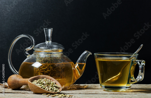 Herbal infusion fennel tea in glass cup  with dried fennel seeds in wooden shovel. Herbal tea alternative medicine background concept.