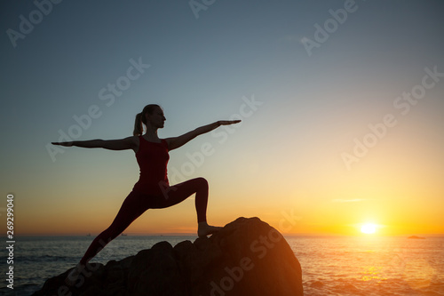 Yoga silhouette young woman doing fitness exercises on the sea beach at amazing sunset.