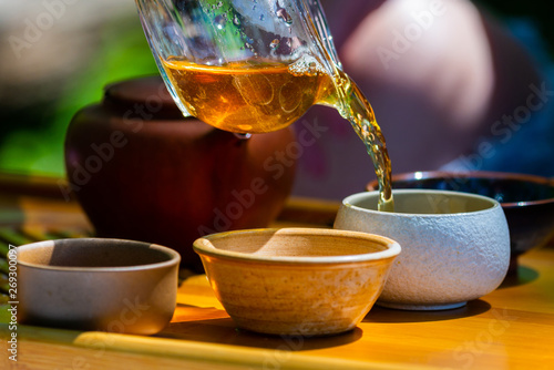 On the table on a wooden tray a teapot with tea, teapot, cups. Man, hands pouring tea