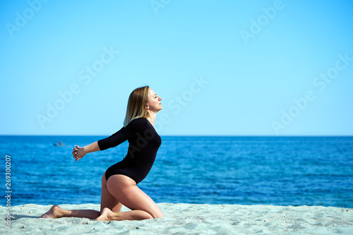 Beautiful woman practices yoga by the sea on a sunny day. The woman does stretching exercises.