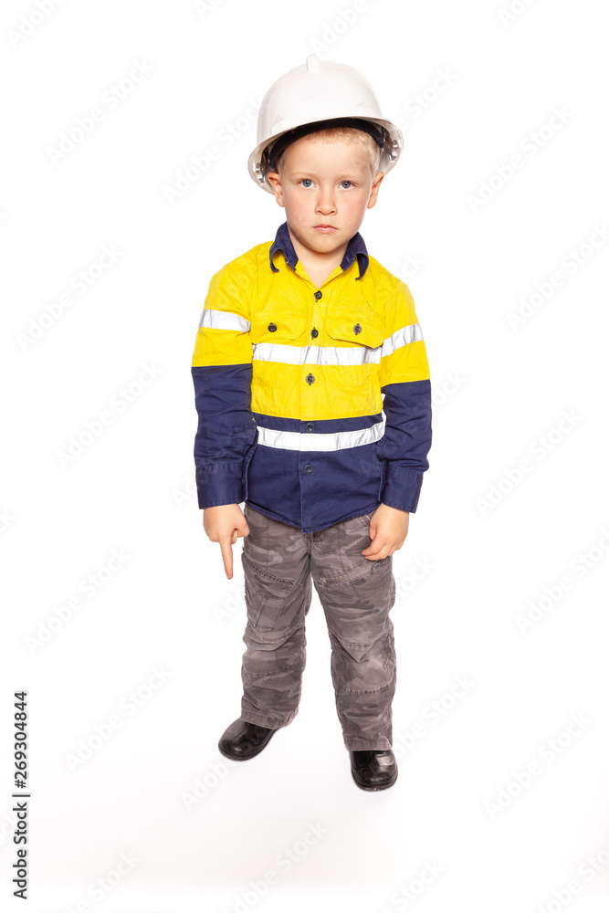 Young blond caucasian boy pointing down with a fierce look role playing a construction worker supervisor in a yellow and blue hi-viz shirt, boots, white hard hat, minus hammer and tape measure Young blond caucasian boy pointing down with a fierce look role playing a construction worker supervisor in a yellow and blue hi-viz shirt, boots, white hard hat, minus hammer and tape measure