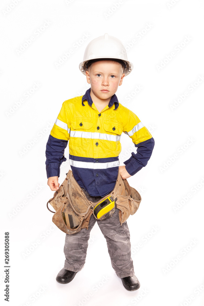Young blond caucasian boy hand on hip role playing as an angry construction worker in a yellow and blue hi-viz shirt, boots, white hard hat, tool belt, a hammer and tape measure. Young blond caucasian boy hand on hip role playing as an angry construction worker in a yellow and blue hi-viz shirt, boots, white hard hat, tool belt, a hammer and tape measure.