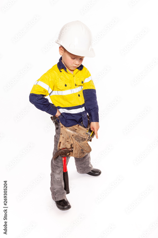 Young blond caucasian boy pointing down with a fierce look role playing a construction worker supervisor in a yellow and blue hi-viz shirt, boots, white hard hat, tool belt, a hammer and tape measure Young blond caucasian boy pointing down with a fierce look role playing a construction worker supervisor in a yellow and blue hi-viz shirt, boots, white hard hat, tool belt, a hammer and tape measure