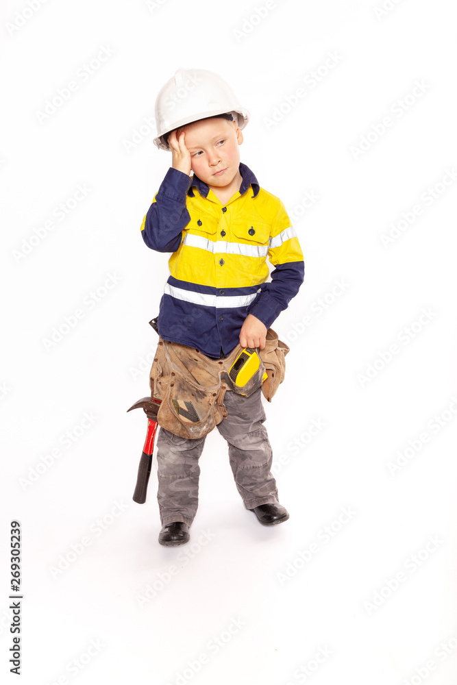 Young blond caucasian boy scratching his head in disbelief role playing a frustrated construction worker in a yellow and blue hi-viz shirt, boots, white hard hat, tool belt, a hammer and tape measure Young blond caucasian boy scratching his head in disbelief role playing a frustrated construction worker in a yellow and blue hi-viz shirt, boots, white hard hat, tool belt, a hammer and tape measure