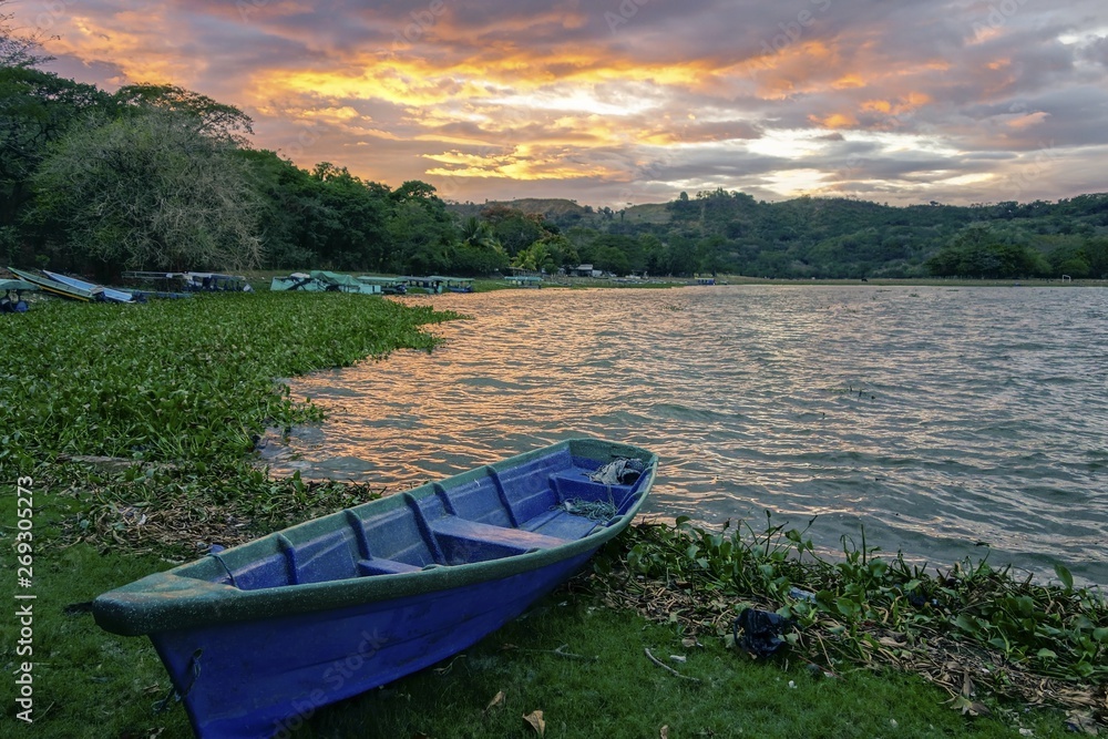 Blue Fishing Boat on Shore of Beautiful Lake Suchitlan and Dramatic Sunset Sky near Town of Suchitoto in El Salvador Blue Fishing Boat on Shore of Beautiful Lake Suchitlan and Dramatic Sunset Sky near Town of Suchitoto in El Salvador