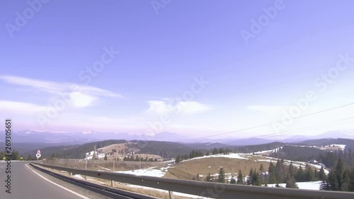 Landscape of Romanian countryside near Toplita. Driving a sunny rural mountain road in winter. Tall trees and blue sky with soft white clouds. photo