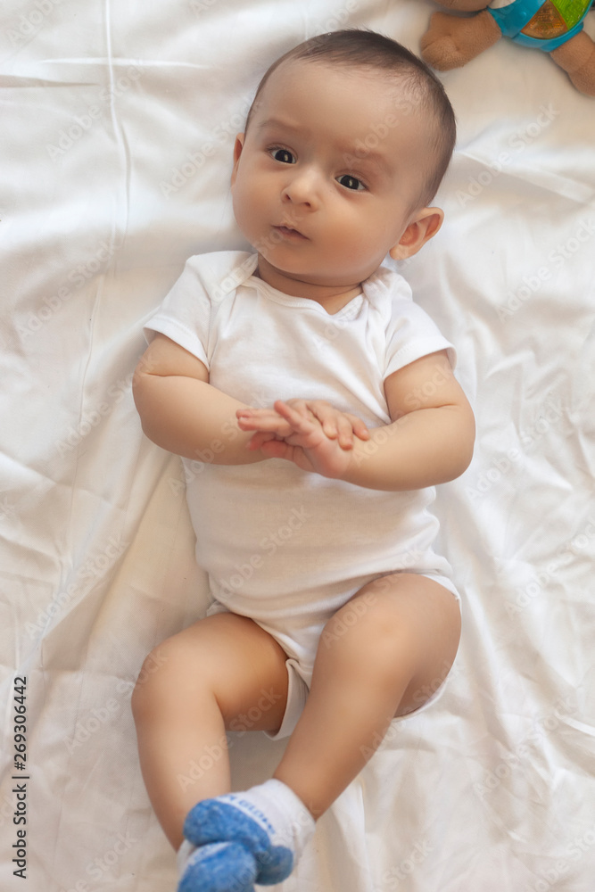 6-8-month-old baby boy lying playfully in bed. Charming 6-7 month little baby in white bodysuit. Baby boy in white bedding. Copy space 6-8-month-old baby boy lying playfully in bed. Charming 6-7 month little baby in white bodysuit. Baby boy in white bedding. Copy space