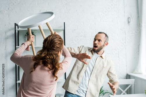 Photography selective focus of surprised man looking at angry holding chair while threatenin