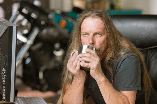 Sleepy Man at his Desk with Coffee and Motorcycle in the Background