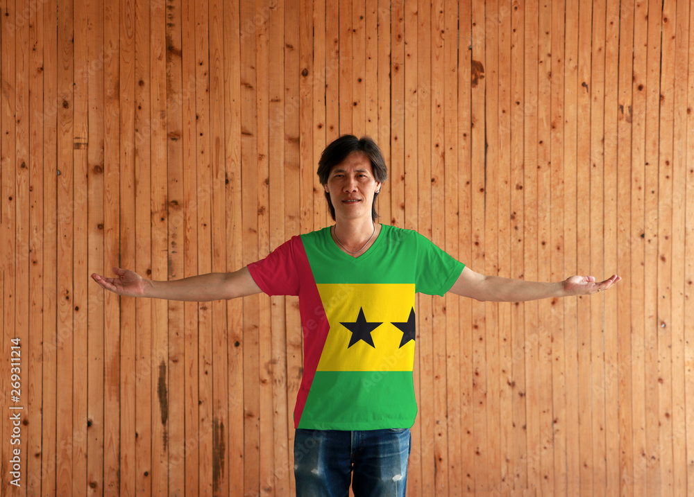 Man wearing Sao Tome and Principe flag color shirt and standing with arms wide open on the wooden wall background. Man wearing Sao Tome and Principe flag color shirt and standing with arms wide open on the wooden wall background.