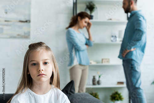 selective focus of upset kid looking at camera near quarreling parents at home