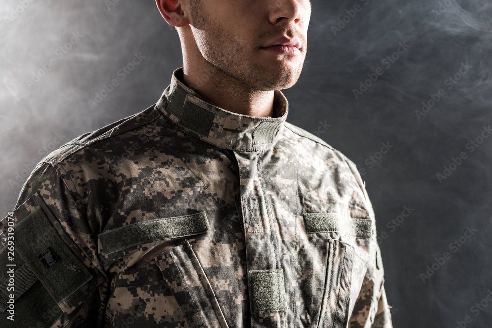 cropped view of serious soldier in military uniform on black with smoke cropped view of serious soldier in military uniform on black with smoke