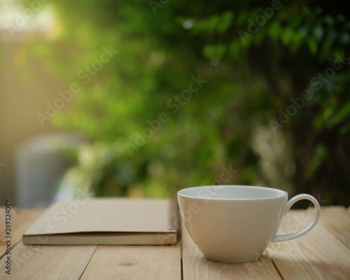 Cup of hot coffee, reading a book on wooden table in the green garden this morning. 