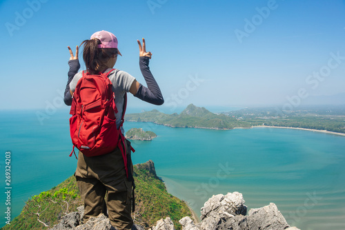 Young traveler woman standing and show hand victory sign on the top of mountain enjoy the beauty of seascape Top View Landscape beach at Prachuab Khirikhan povince Thailand. photo