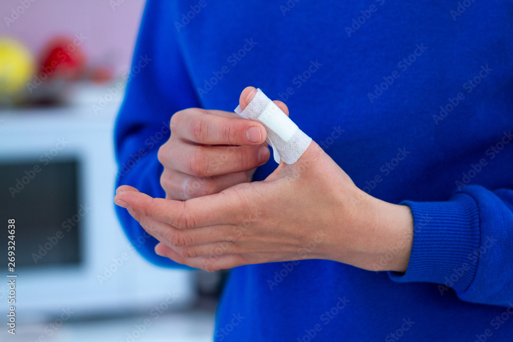 Woman using a medical sticking plaster for injured finger. First band aid for cuts and wounds