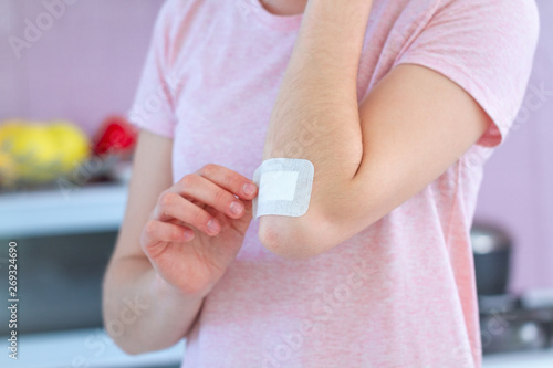 Woman putting an adhesive plaster on injured elbow at home. First aid for cuts and wounds