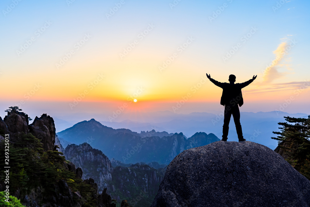 Hiker is standing on a rock with raised hands and enjoying sunrise