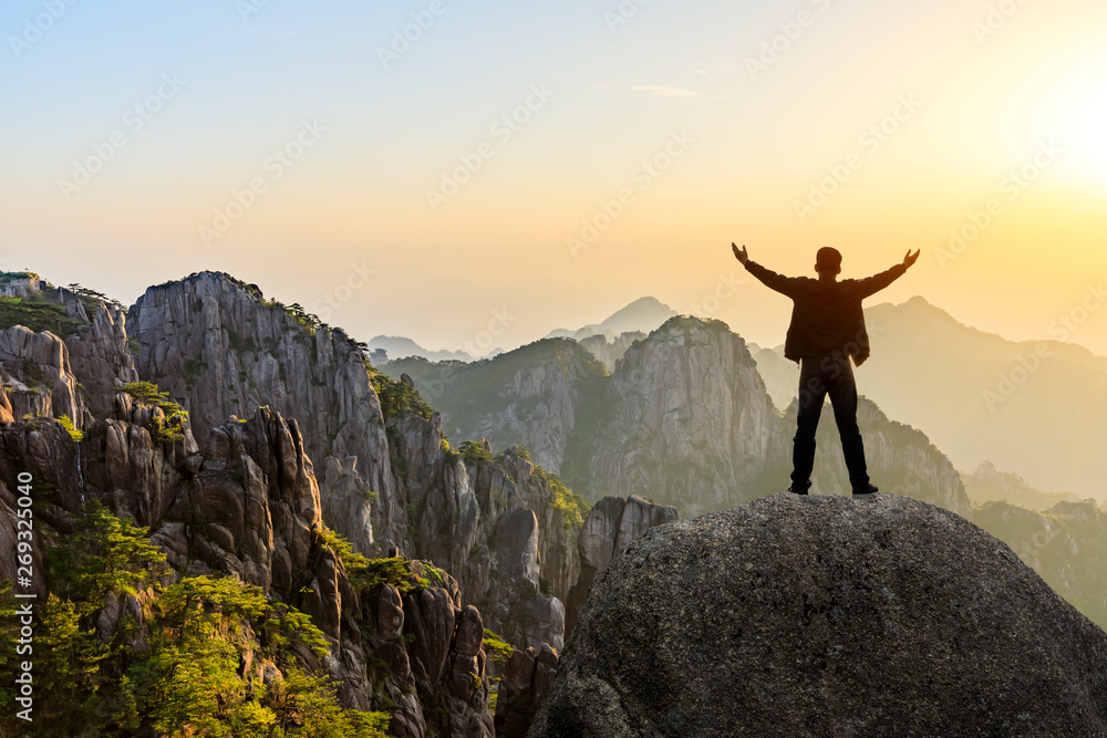 Hiker is standing on a rock with raised hands and enjoying sunrise