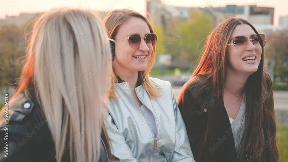 Friends leisure. Beautiful happy girls hanging out in city park at sunset. Ladies sitting, chatting, laughing. Blur background. Friends leisure. Beautiful happy girls hanging out in city park at sunset. Ladies sitting, chatting, laughing. Blur background.