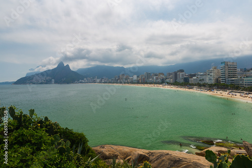 Ipanema beach is adjacent to Copacabana and Leblon Beach, surfers in ocean and sun bathers on sandy beach and Two Brothers mountain rise at the western end of the beach, Rio de Janeiro, Brazil. 