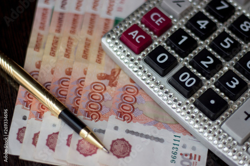 calculator with rhinestones, banknotes 5000 rubles and a gold pen on a dark background