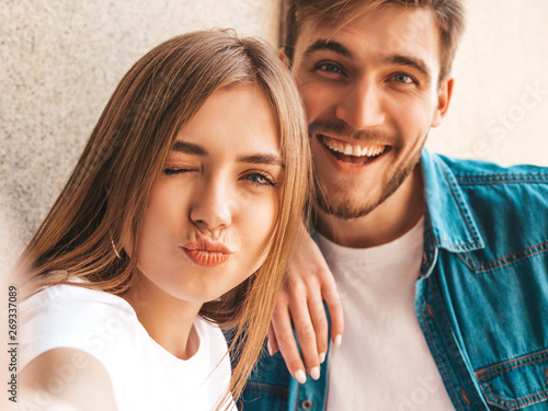 Smiling beautiful girl and her handsome boyfriend in casual summer clothes. Happy family taking selfie self portrait of themselves on smartphone camera. Having fun and making duck face