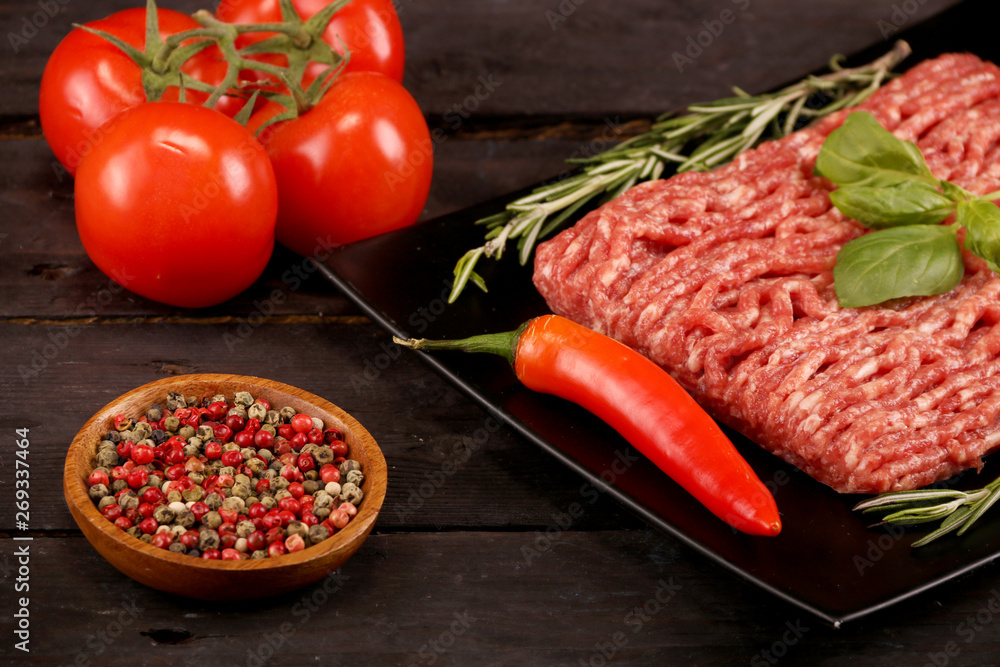 raw minced meat on paper, ingredients for burger with tomato, pepper, onion, spices and seasonings on black background raw minced meat on paper, ingredients for burger with tomato, pepper, onion, spices and seasonings on black background