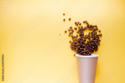 Fototapeta Naklejka Na Ścianę i Meble -  Roasted coffee grains and takeaway cup top view. Craft paper tea cup on orange background flat lay. Cafe web banner with copyspace