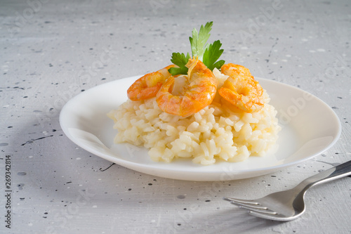Risotto with shrimps and parsley on a white plate on a light gray background with copy space. Italian food