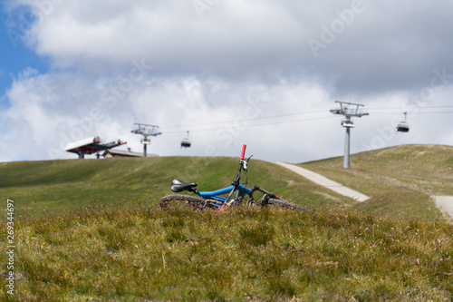 Full suspension downhill mountain bike lying on ground, mountains over Livigno with cableway in backround, sunny summer day, Italy photo