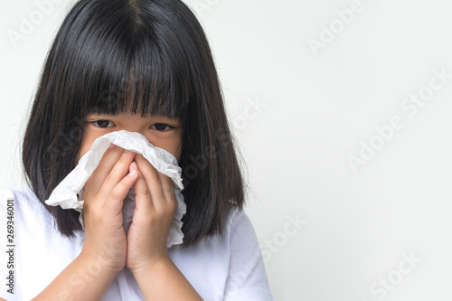 Portrait of unhealthy sick Asia kid girl standing with napkin close her nose from allergy or rhinitis. Unhappy ill child suffering from running nose and sneezing and blow her nose on white background